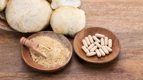 Best Lion’s Mane Supplement. Lion’s mane mushrooms, mushroom powder and capsules are on a wood table in wood bowls.