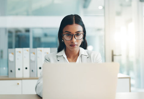 A woman wearing glasses working intently at a laptop after taking amino acids for focus and attention.