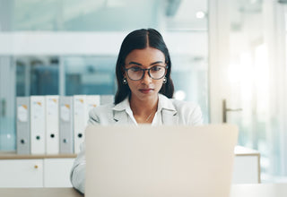 A woman wearing glasses working intently at a laptop after taking amino acids for focus and attention.