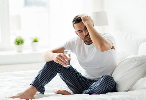 Man in pyjamas nursing a hangover with nootropics and a glass of water.