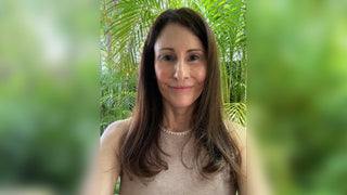Awoman with long dark hair smiles against a lush green tropical background.