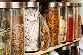 Adaptogen Side Effects: What You Need to Know. Glass cylinder bottles filled with various herbs on a shelf.