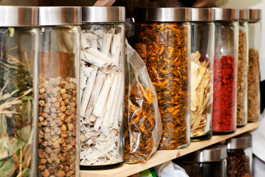 Adaptogen Side Effects: What You Need to Know. Glass cylinder bottles filled with various herbs on a shelf.